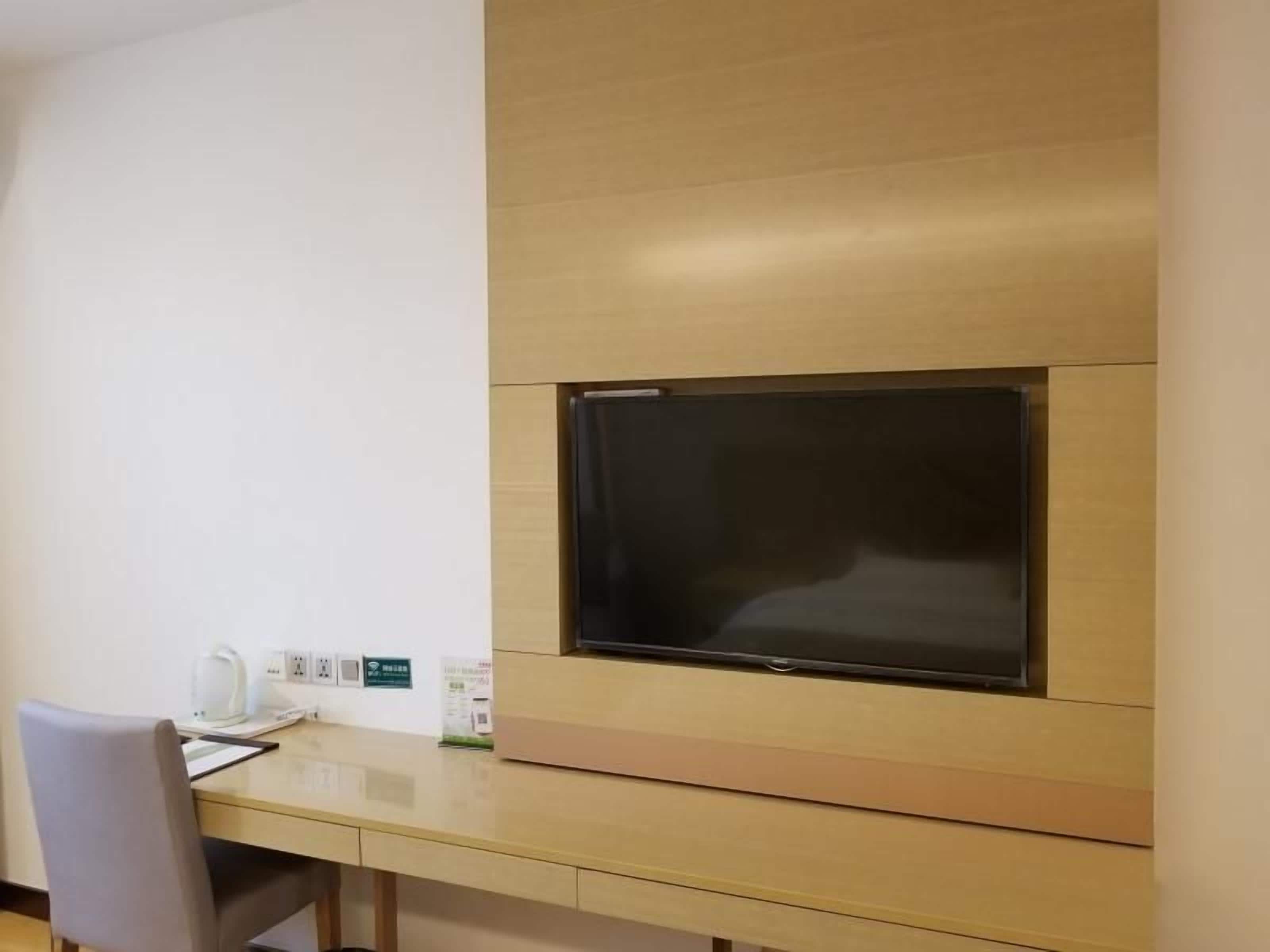 A modern room with a flat-screen TV mounted on the wall, a wooden desk, and a chair.