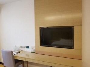 Una habitación moderna con una televisión de pantalla plana en la pared, un escritorio de madera y una silla.