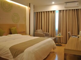 A hotel room with a large bed, a chair, a small table with a drink, and a window with curtains.