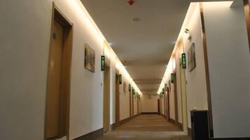 A hotel hallway with doors marked by green signs, a carpeted floor, and a ceiling with recessed lighting.