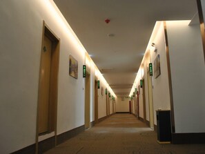 Pasillo de hotel con puertas señalizadas con letreros verdes, suelo alfombrado e iluminación empotrada en el techo.