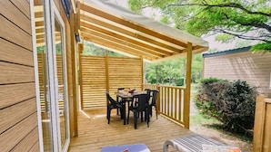 Una terraza de madera con un porche cubierto, una mesa con sillas y un banco.