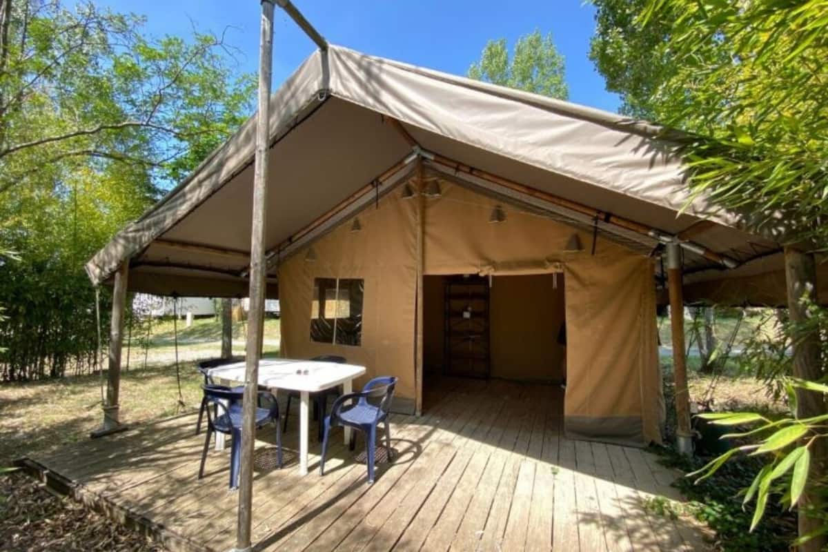 Un espacio al aire libre con carpas, una mesa y sillas, rodeado de árboles.