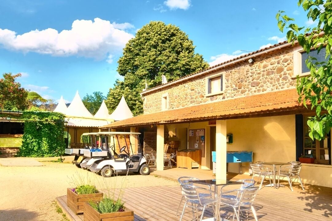 A stone building with a patio area, clear chairs, and a golf cart.