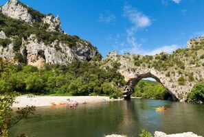 A natural landscape with a river, a sandy beach, and a rock arch formation. - Ludo Camping Parc (Lussas)
