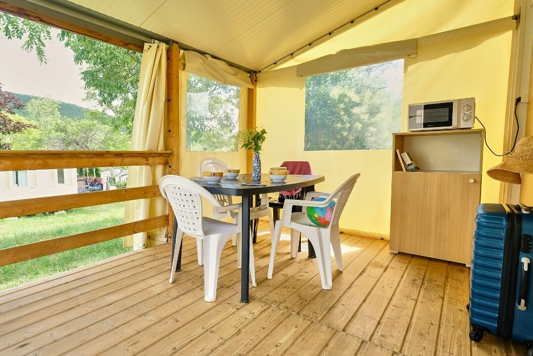 A room with a wooden deck, a round table with chairs, a microwave, and a small cabinet.