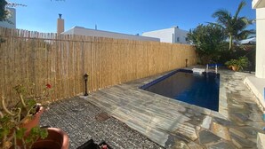 En trädgård med en pool, ett bambustaket och en stenbelagd uteplats.