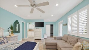 A bedroom with a bed, a ceiling fan, a TV, a dresser, a couch, and a window with blinds. - Eden's Reef : 3bed/3bath (Lauderdale by the Sea)