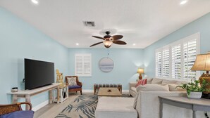 A living room with a ceiling fan, a flat-screen TV, wicker furniture, a sofa, and a coffee table. - Eden's Reef : 3bed/3bath (Lauderdale by the Sea)