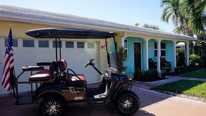 A golf cart parked in front of a house with a garage, a porch with chairs, and an American flag. - Eden's Reef : 3bed/3bath (Lauderdale by the Sea)