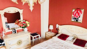 Une chambre à coucher avec un lit blanc, une commode, un miroir, une table de chevet et un mur rouge.