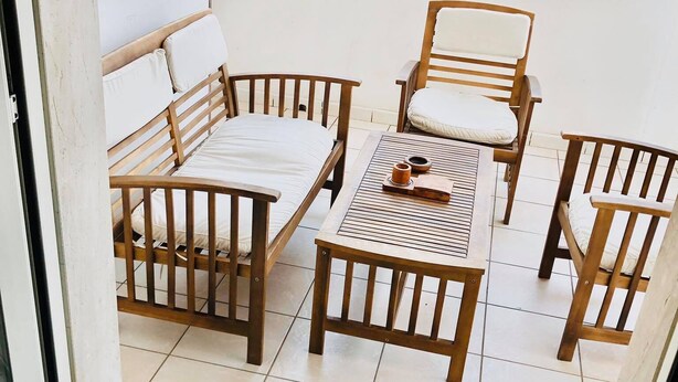 Un balcon avec une table et des chaises en bois, un canapé et un petit objet décoratif posé sur la table.
