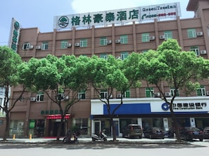 Un hotel con un cartel, una calle bordeada de árboles y un banco al otro lado de la calle.