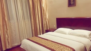 Ein Hotelzimmer mit Bett, Vorhängen, einem Nachttisch und einem gerahmten Bild an der Wand.