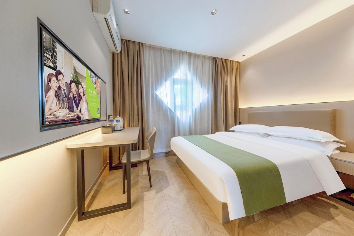 Habitación de hotel con cama, escritorio, silla, televisor y ventana con cortinas.