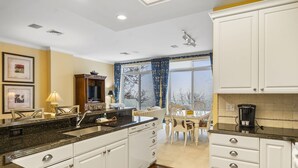 Una cocina moderna con armarios blancos, encimera de granito y un comedor con mesa y sillas.