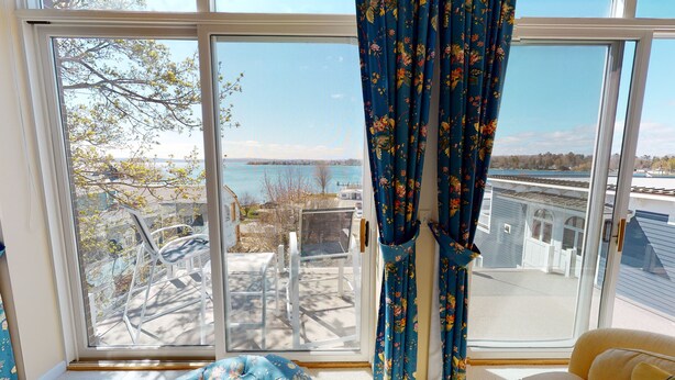 Una habitación con un gran ventanal corredero que da a un balcón con vistas a un lago y árboles.