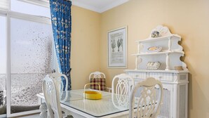 Un comedor con una mesa de vidrio, sillas blancas, una cesta amarilla y un armario blanco con adornos.