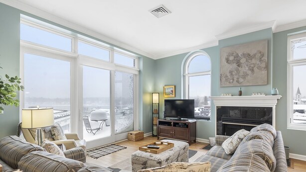 Ein geräumiges Wohnzimmer mit großem Fenster, Kamin, Fernseher und einer Sofagarnitur.