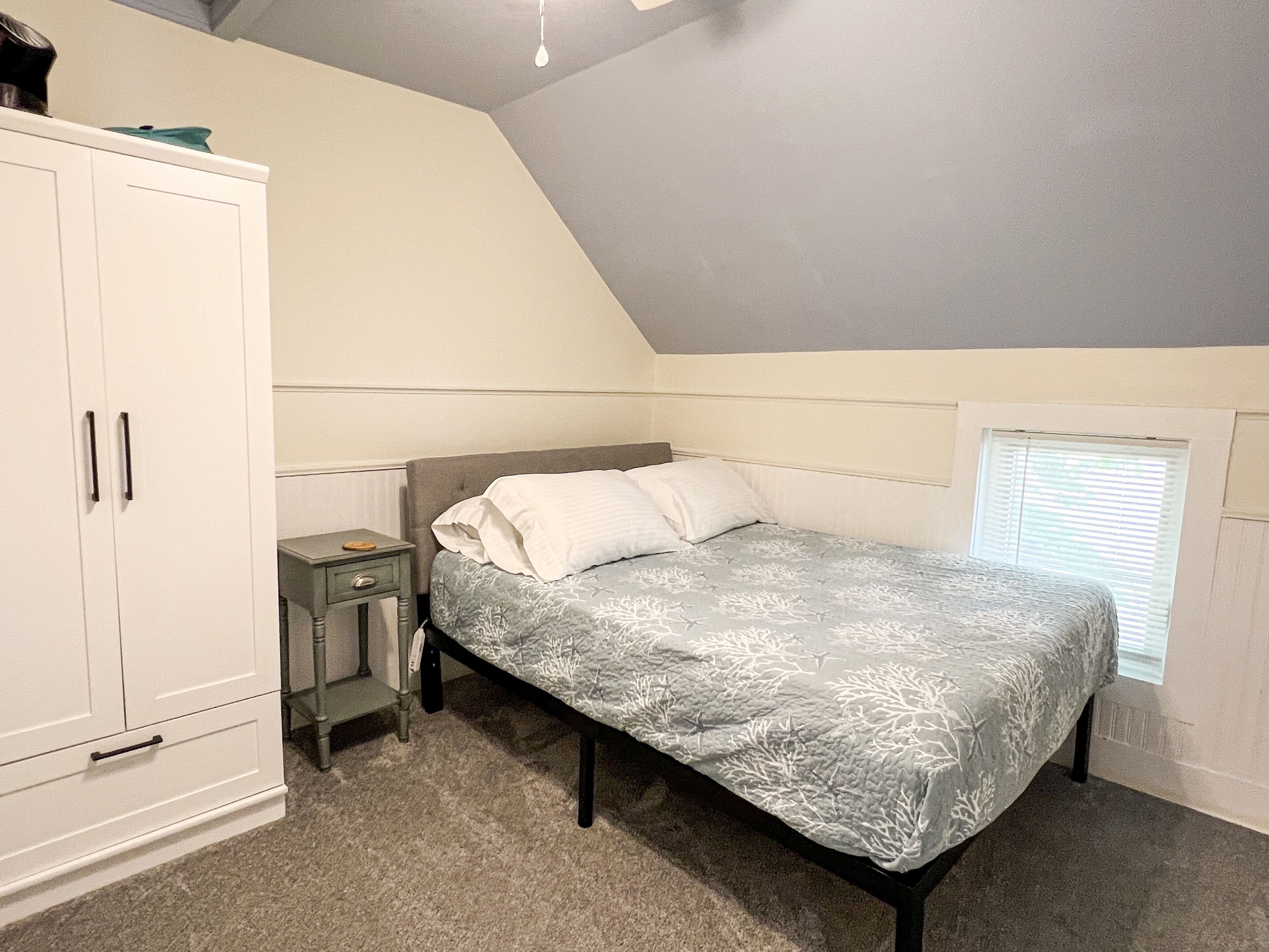 Quarto com cama, mesa de cabeceira, guarda-roupa e janela.