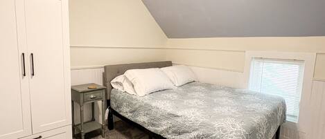 Quarto com cama, mesa de cabeceira, guarda-roupa e janela.