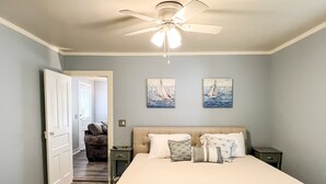 Une chambre avec un grand lit, un ventilateur de plafond et deux tableaux accrochés au mur.