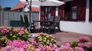 Um pátio com mesa e cadeiras, rodeado por flores cor-de-rosa.