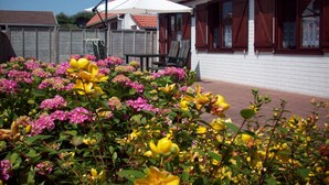 Um jardim com flores rosa e amarelas em frente a um edifício com telhado vermelho e paredes brancas.