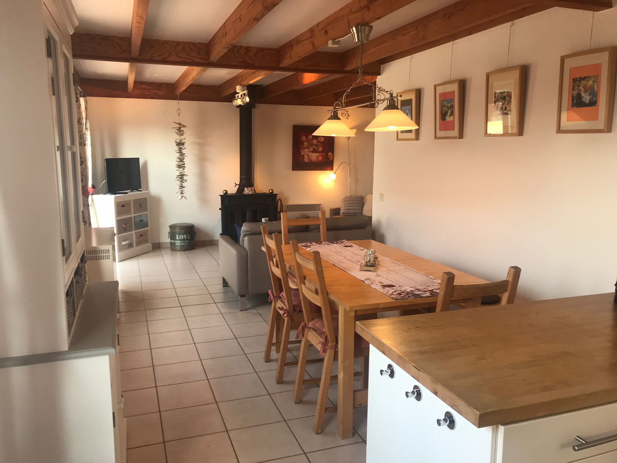 Un rincón comedor acogedor con una mesa y sillas de madera, una estufa negra y cuadros en la pared.