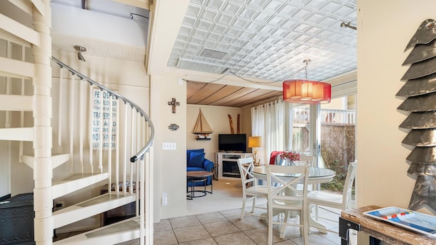 A spacious living area with a staircase, a dining table with chairs, a television, and a decorative sailboat.