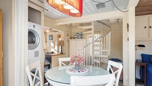 A round glass table with white chairs, a vase with flowers, and a washing machine in the background.