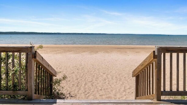 A wooden deck leading to a sandy beach with a clear view of the water.