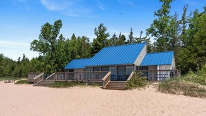 A beach house with a blue roof, wooden deck, and stairs leading to the entrance.