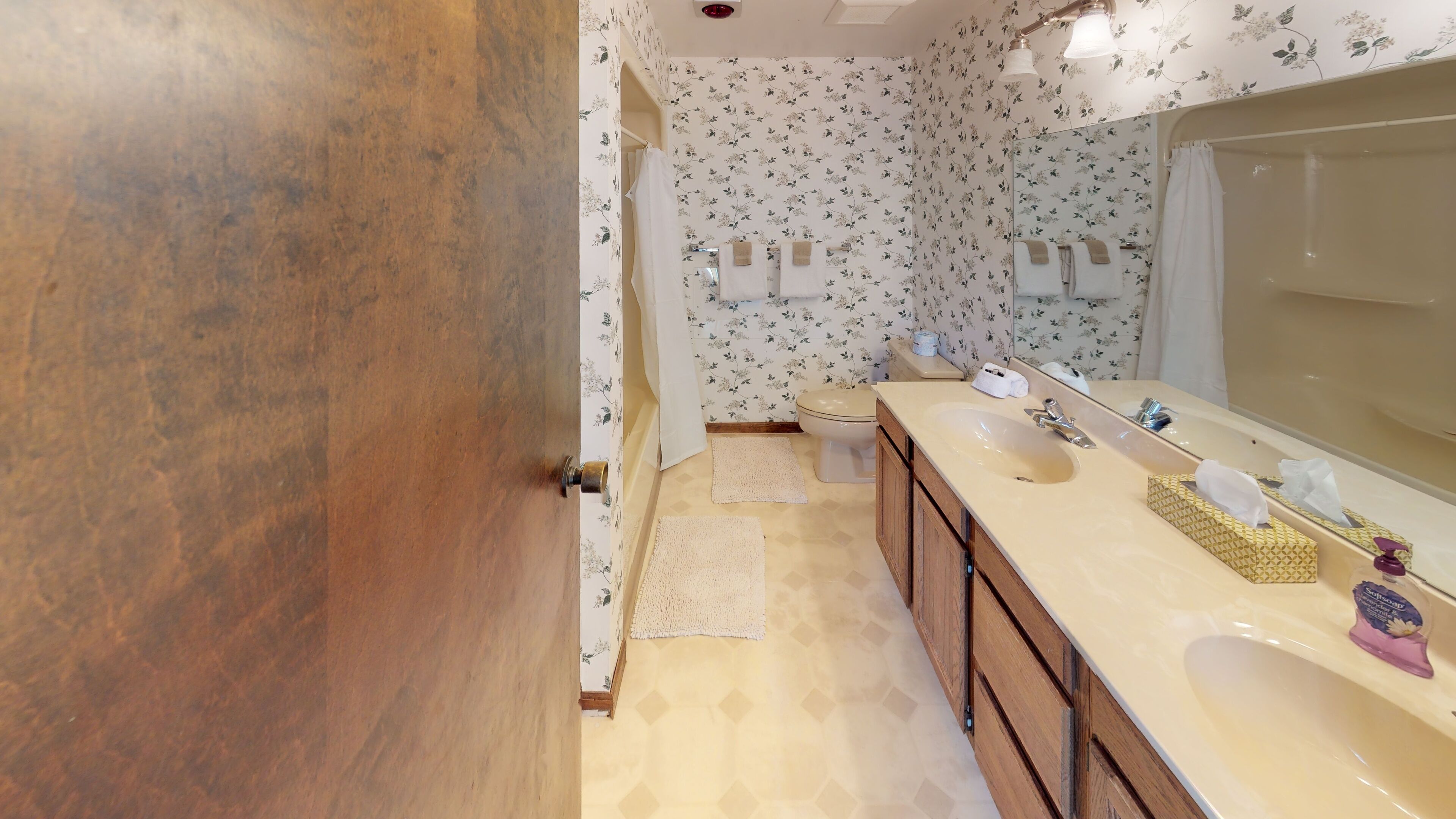 Un baño con puerta de madera, un lavabo color beige con espejo y un inodoro.