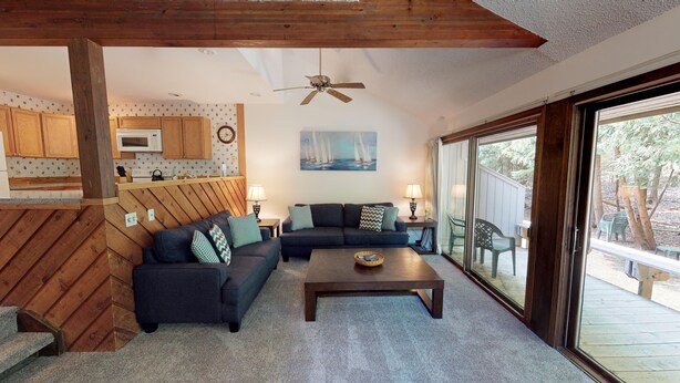 A cozy living room with a dark sofa, a wooden coffee table, and a view of the outdoors through large sliding glass doors. - Harbor Cove! 5 Bedroom! #82 Ski, Golf, Shop! (Harbor Springs)