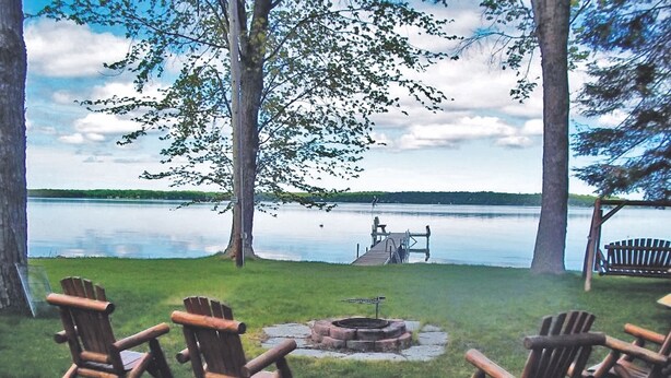 Järvenrantainen oleskelualue, jossa on Adirondack-tyylisiä tuoleja ja nuotiopaikka.