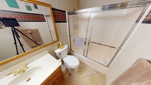 Ein Badezimmer mit weißem Waschbecken, Toilette, Duschkabine und einem Spiegel mit dekorativem Rahmen.