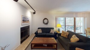 Un salon doté d’une cheminée, de deux canapés, d’une table basse en bois et offrant une vue sur un balcon aménagé avec du mobilier d’extérieur.