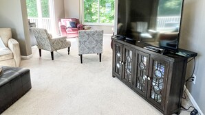 A living room with a large flat-screen TV on a dark wooden cabinet, two patterned armchairs, a beige sofa, and a red couch. - COMFORTABLE & SPACIOUS Home in Harbor Springs - Minutes from the Ski Hills!! (Harbor Springs)