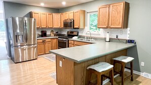 A modern kitchen with wooden cabinets, stainless steel appliances, and a large island with bar stools. - COMFORTABLE & SPACIOUS Home in Harbor Springs - Minutes from the Ski Hills!! (Harbor Springs)