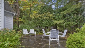 Eine Terrasse im Freien mit Steinboden, weißen Metallstühlen und einem Tisch.