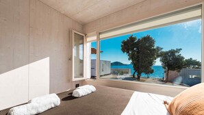 A modern hotel room with a large window offering a view of the sea and trees. - Buqez - 2BR - Beach Villa 42 (Pakostane)