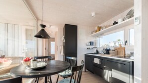 A modern kitchen with a round dining table, dark cabinetry, and a view of the outside. - Buqez - 2BR - Beach Villa 42 (Pakostane)