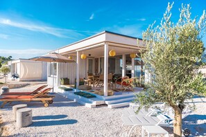 A covered outdoor seating area with lounge chairs and tables, a gravel ground, and a tree. - Buqez - 2BR - Beach Villa 42 (Pakostane)