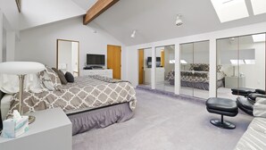 Une chambre moderne avec un grand lit, un bureau, une chaise et un dressing doté d’un miroir.