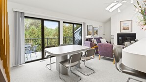 Un salon moderne doté d’une grande table à manger, de sièges confortables, d’une cheminée et d’un balcon aménagé avec du mobilier d’extérieur.