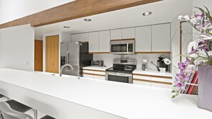 Une cuisine moderne avec des meubles blancs, des appareils en acier inoxydable et une poutre en bois au plafond.