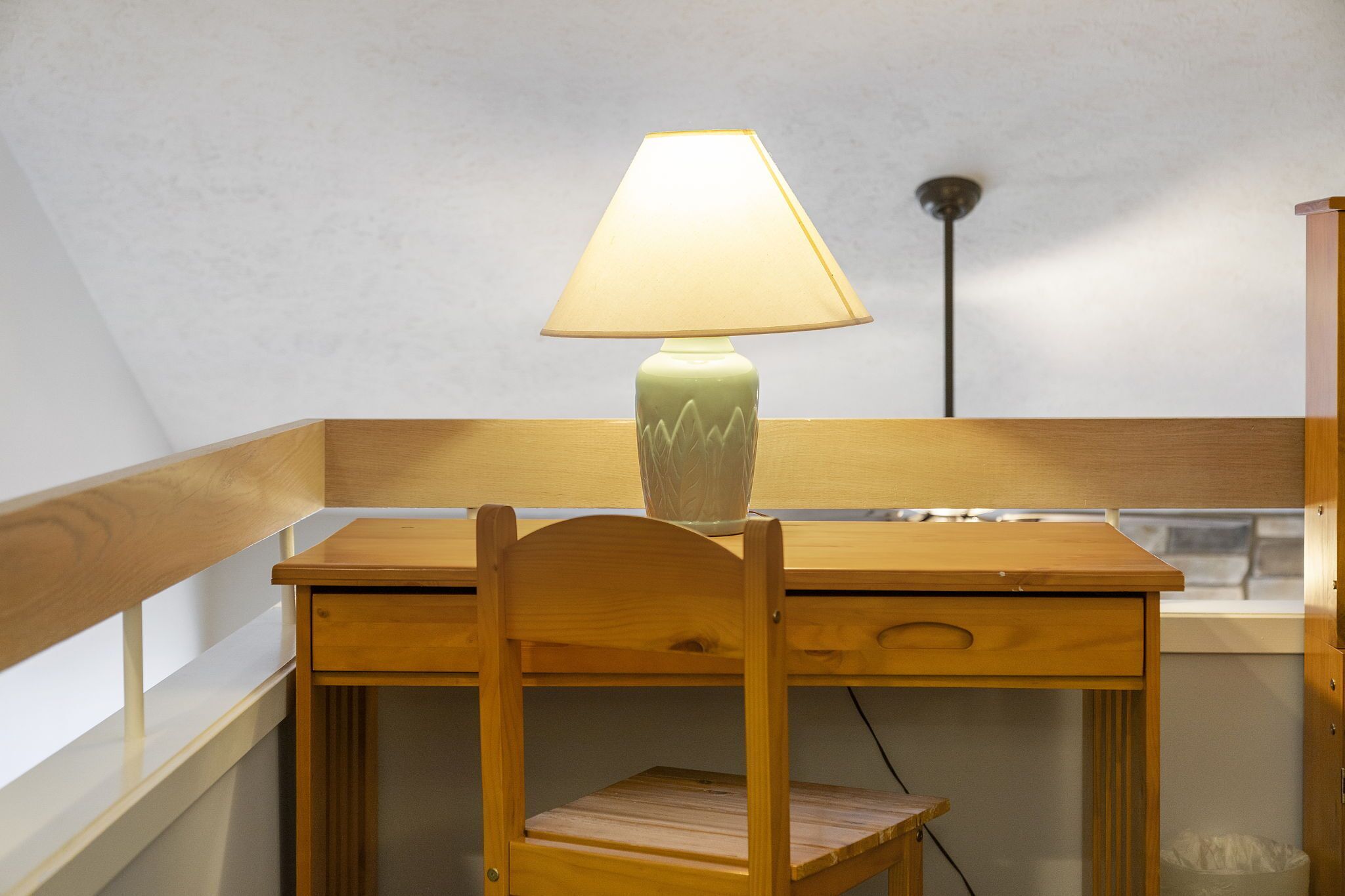A wooden desk with a lamp in a room with a sloped ceiling.