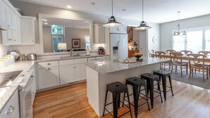Une cuisine moderne avec des meubles blancs, un grand îlot central doté de tabourets et un éclairage suspendu.