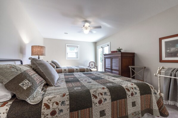 A bedroom with a large bed, a ceiling fan, a dresser, and a window.
